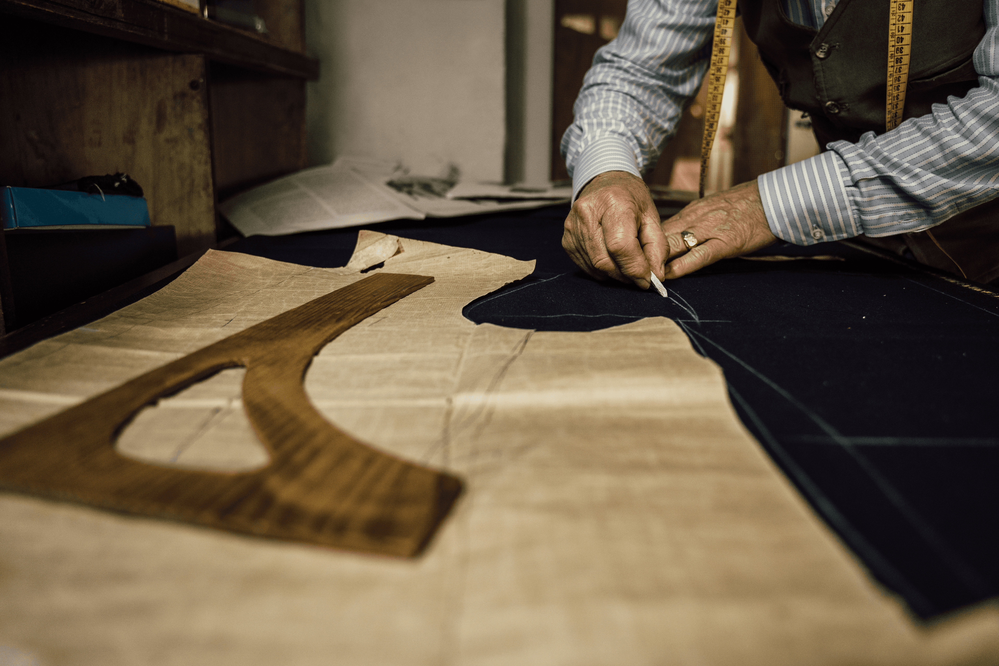 Master tailor cutting cloth pattern by hand on the atelier workbench