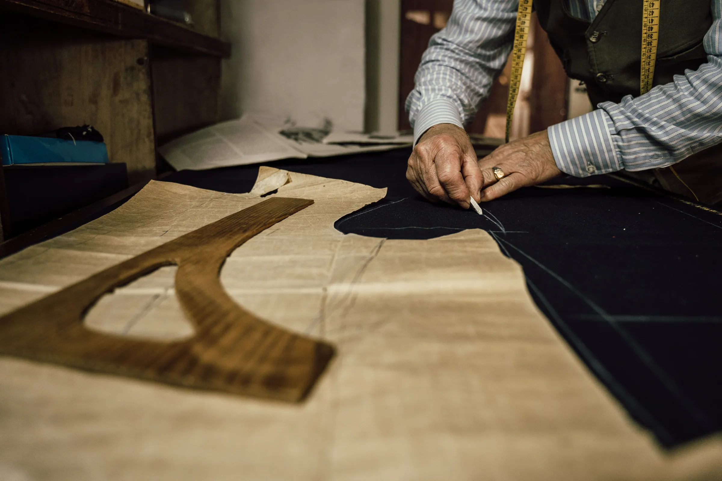 Master tailor cutting cloth pattern by hand on the atelier workbench